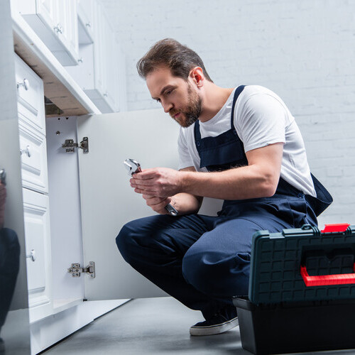 handyman with pair of nippers checking sink in kitchen